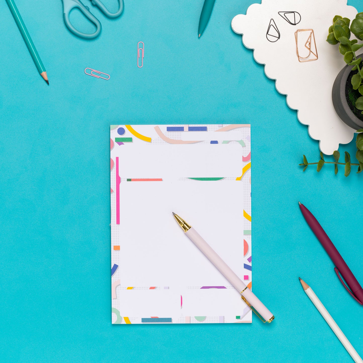 Cutouts A5 Daily Planner Pad on a teal desk, with pens, a white keyboard and a small plant around it.