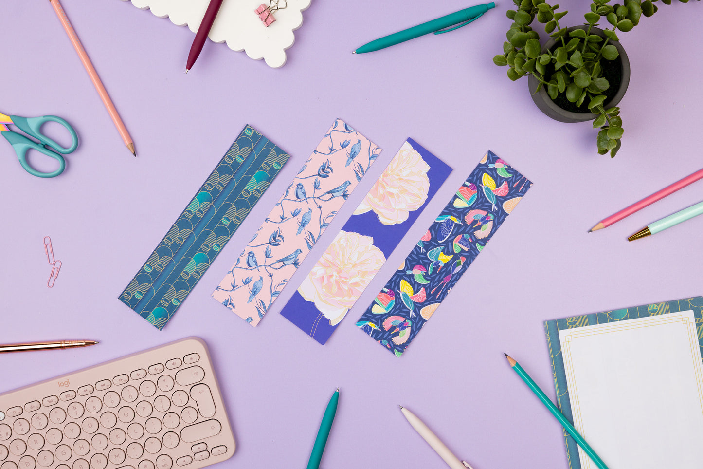 Birds-eye view of the full bookmark set, with the full-colour pattern sides facing up.  They are on a lilac desk with books, pens a light pink keyboard and a notepad around them. 