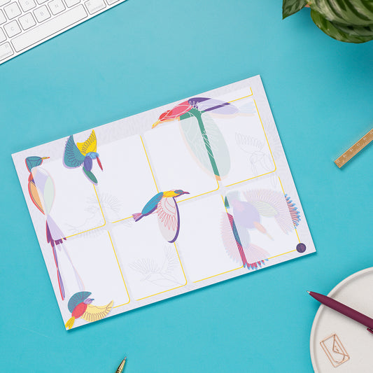 Paradise A4 Planner Pad (8 blocks with bird illustrations around/across it) laid on a teal desk with pens and a white keyboard around it.