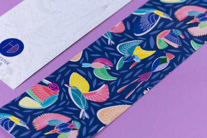Close up of the full-colour patterned side of the Paradise with a navy background, the line drawn motifs and the colour blocks behind.  Next to it is an out of focus corner of the bookmark's other side. They are on a lilac desk.