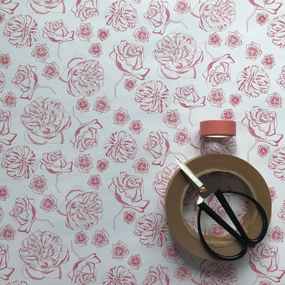 Spring Forward wrapping paper - white background with dark pink line-drawn floral motifs - is flat on a table.  To the bottom right there is a small pair of scissors, small roll of pink tape and a larger roll of brown tape piled up on it.