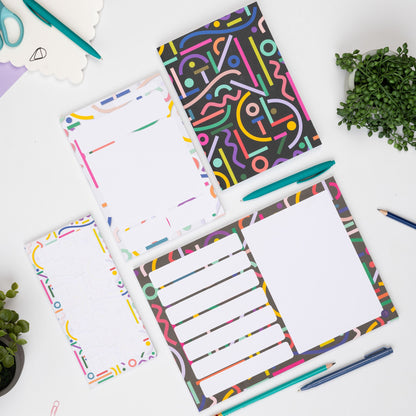 Birds eye view of the Cutouts Full Collection - A4 Planner pad, List Pad, A5 Daily Planner and A5 Dot grid notebook - laid flat on a white desk with pens and paperclips around them as well as two small plants.