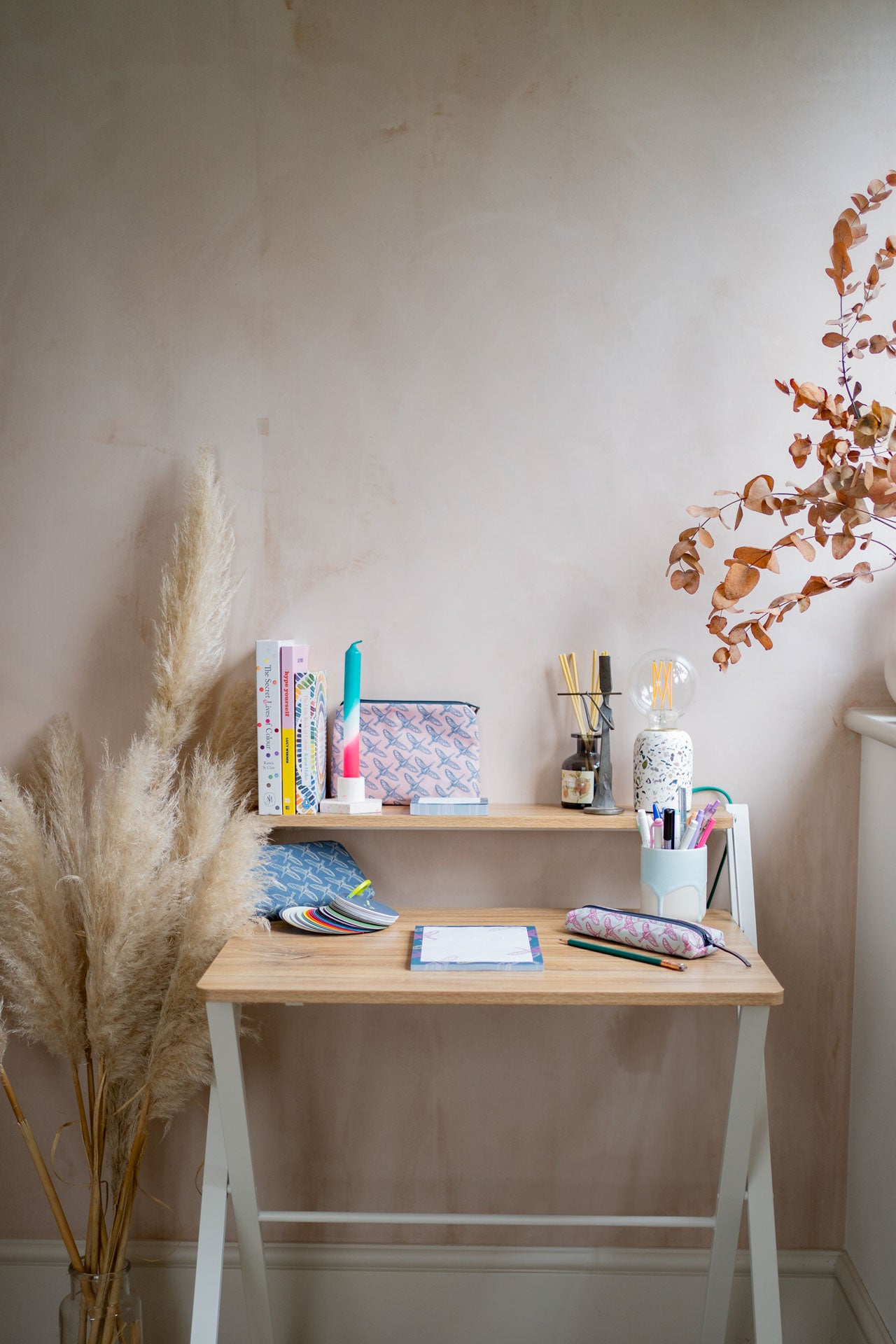 Small wooden desk with Holchester Designs stationery items against a bare plaster wall