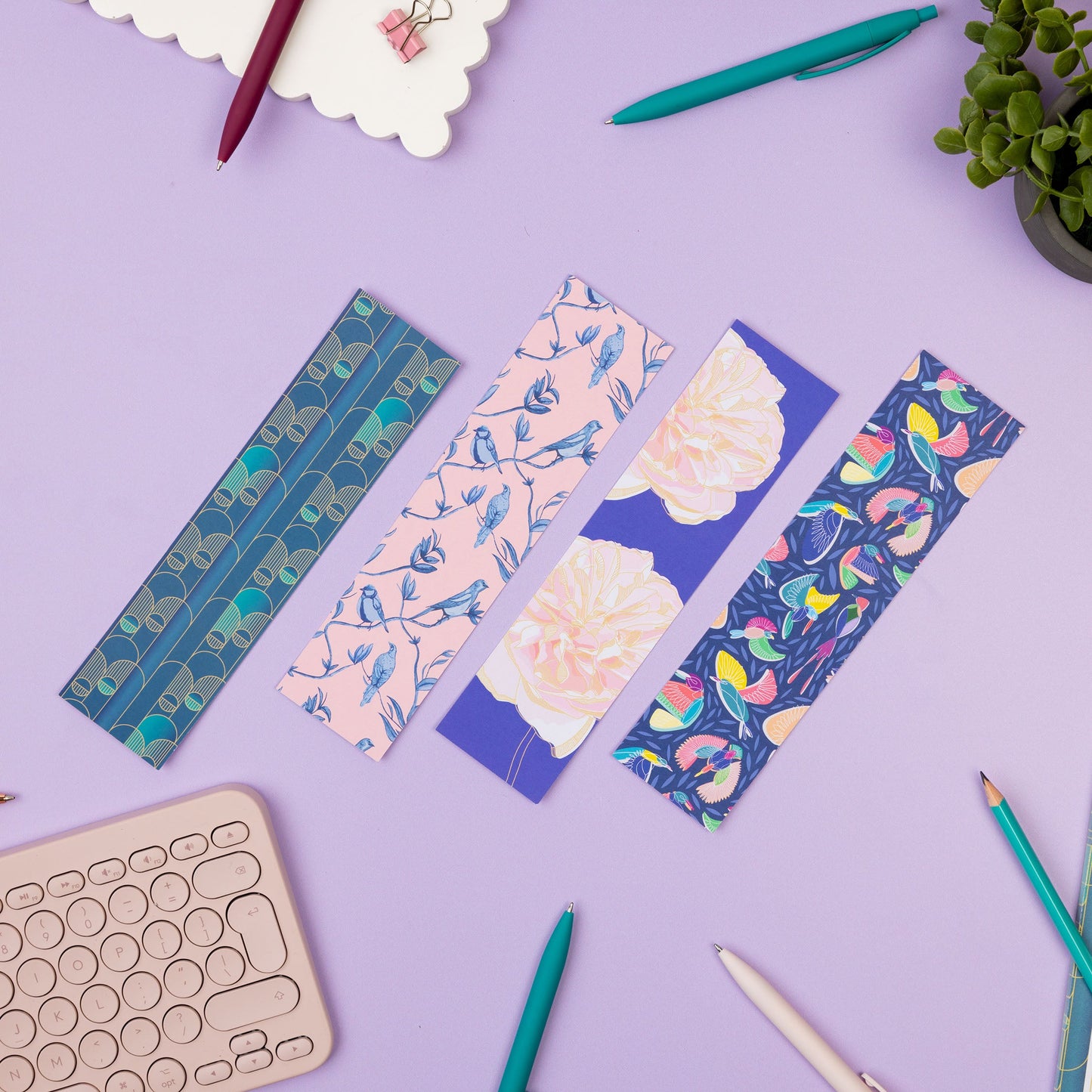 Birds-eye view of the full bookmark set, with the full-colour pattern sides facing up.  They are on a lilac desk with books, pens a light pink keyboard and a notepad around them. 
