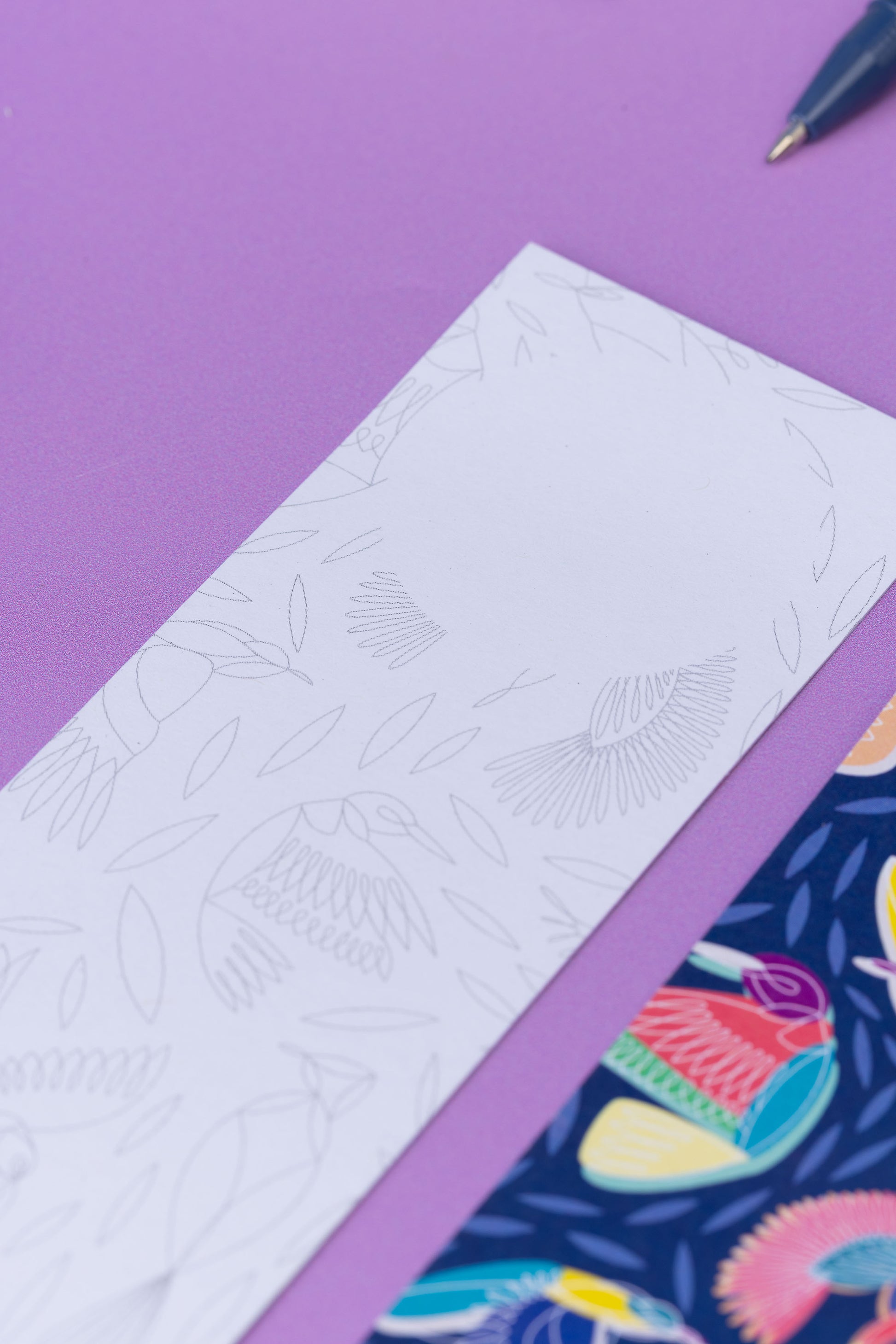 Two of the paradise double-sided bookmarks, on a lilac desk. The main focus is on the top of the monochrome side of the bookmark, with the blank circle for writing at the top of the marker.  The full-pattern side of the bookmark is in the bottom right corner slightly out of focus.